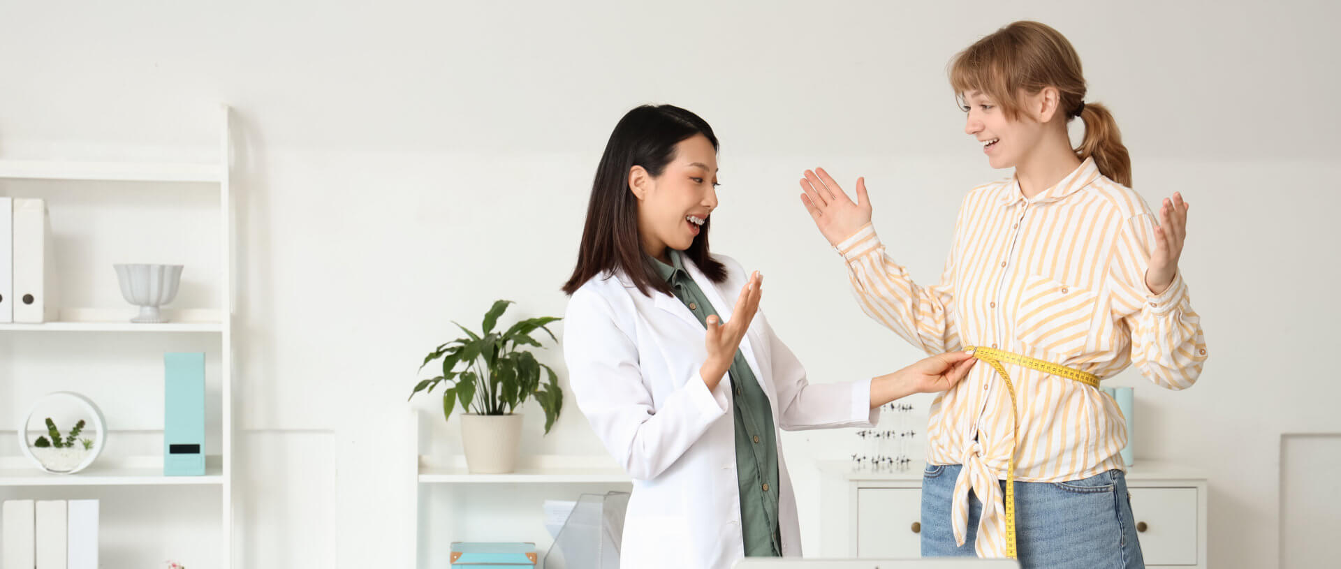 Female Asian nutritionist measuring patient's waist in office